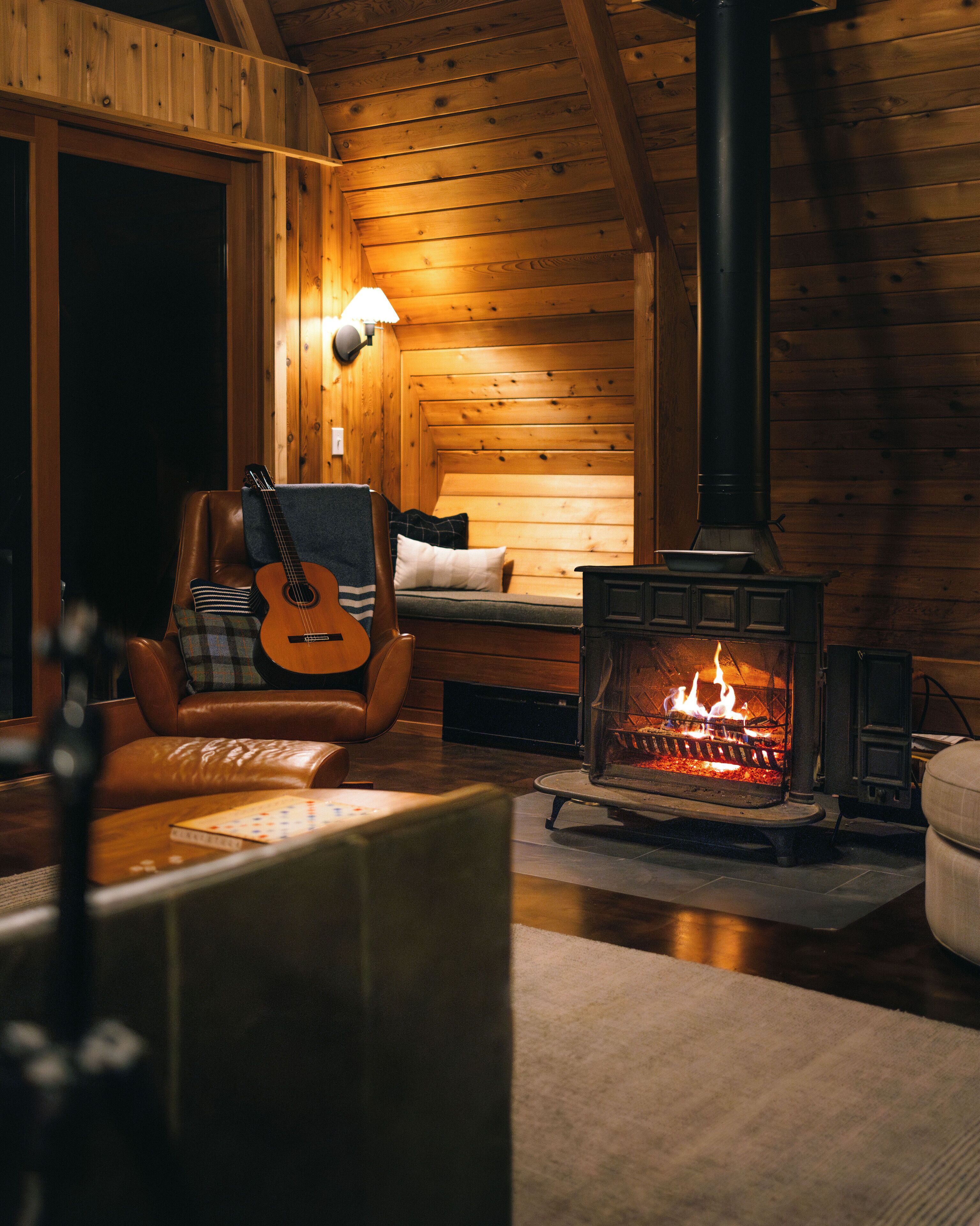 A cozy cabin interior with a wooden interior, a fireplace, a leather armchair, and a guitar.