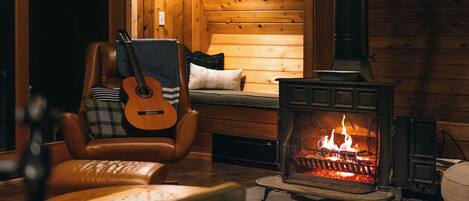 A cozy cabin interior with a wooden interior, a fireplace, a leather armchair, and a guitar.