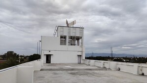Una terraza en la azotea con un edificio blanco, una escalera y vistas a montañas distantes.