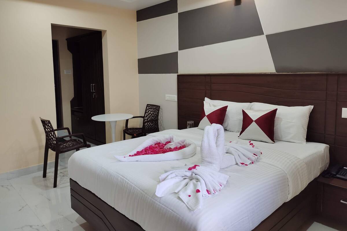 A hotel room with a neatly made bed, a small table, two chairs, and a wall with a geometric pattern.