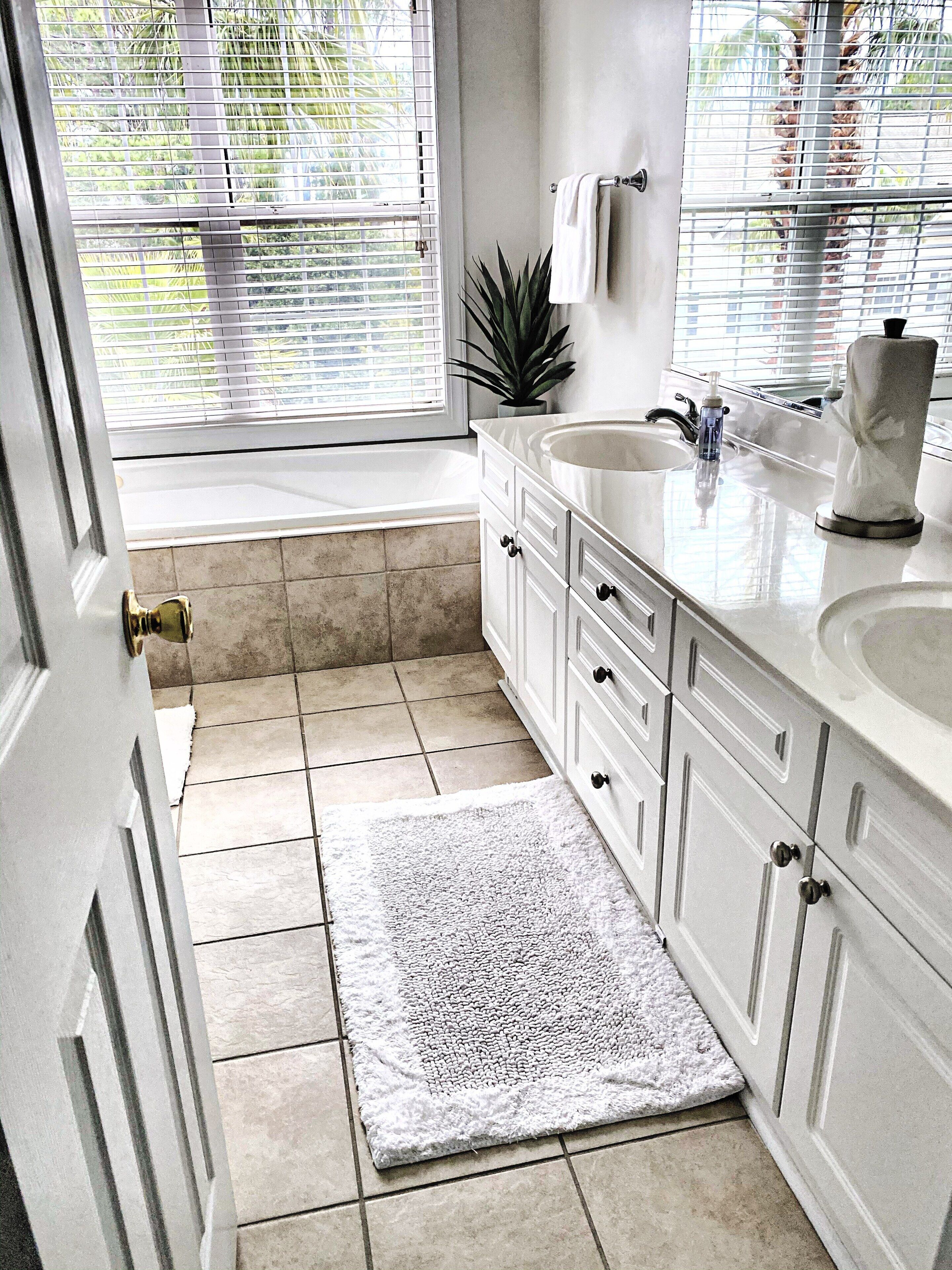 A bathroom with a bathtub, a sink, and a window with blinds.