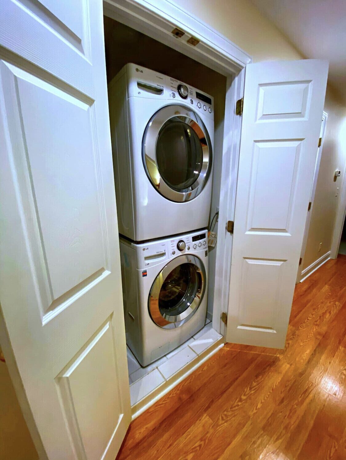 A laundry room with a stacked washer and dryer, wooden flooring, and white doors.