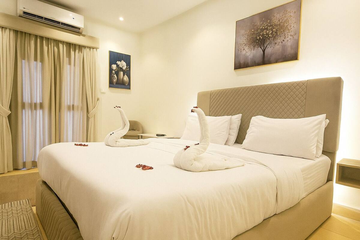 A hotel room with a large bed, a headboard, a nightstand, and a painting on the wall.