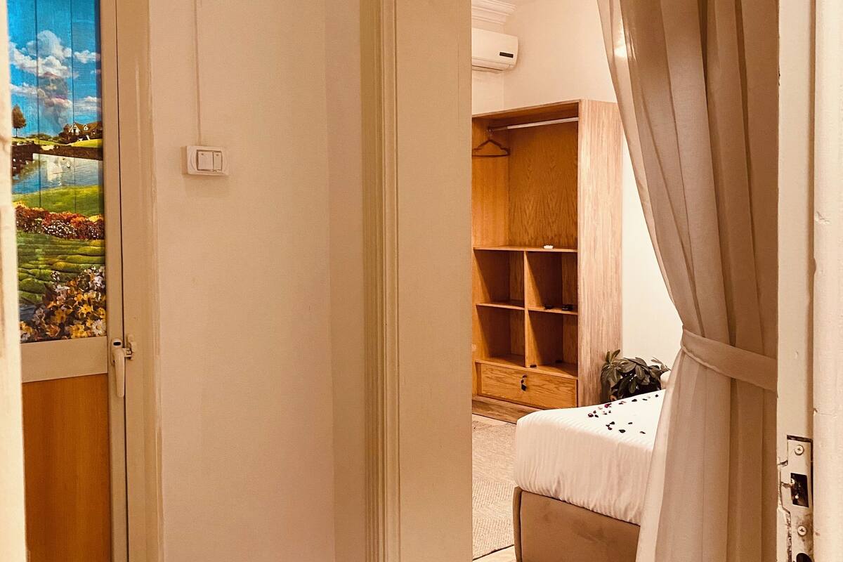 A bedroom with a bed, a wooden wardrobe, and a small desk.
