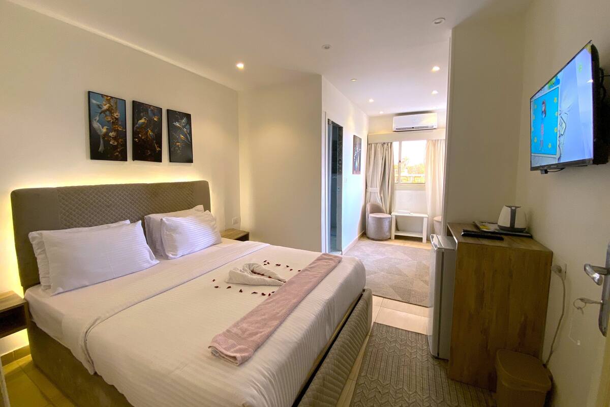 A hotel room with a large bed, a bedside table, a TV, and artwork on the wall.