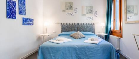 A bedroom with a bed, a nightstand, a lamp, and artwork on the walls.
