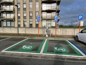 A parking area with designated spaces for disabled parking and electric vehicle charging, in front of a modern building with multiple balconies.