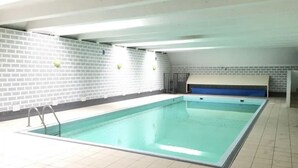 Una piscina interior con piso y paredes de azulejos, un banco azul a lo largo de un lado y un techo con vigas a la vista.