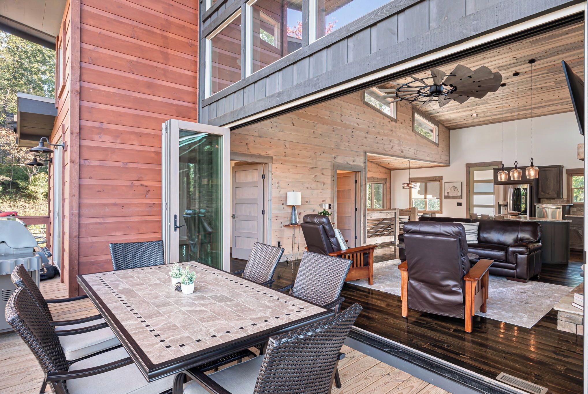 A modern house with a wooden exterior, a dining area with a table and chairs, a living room with a sofa and chairs, and a kitchen area.