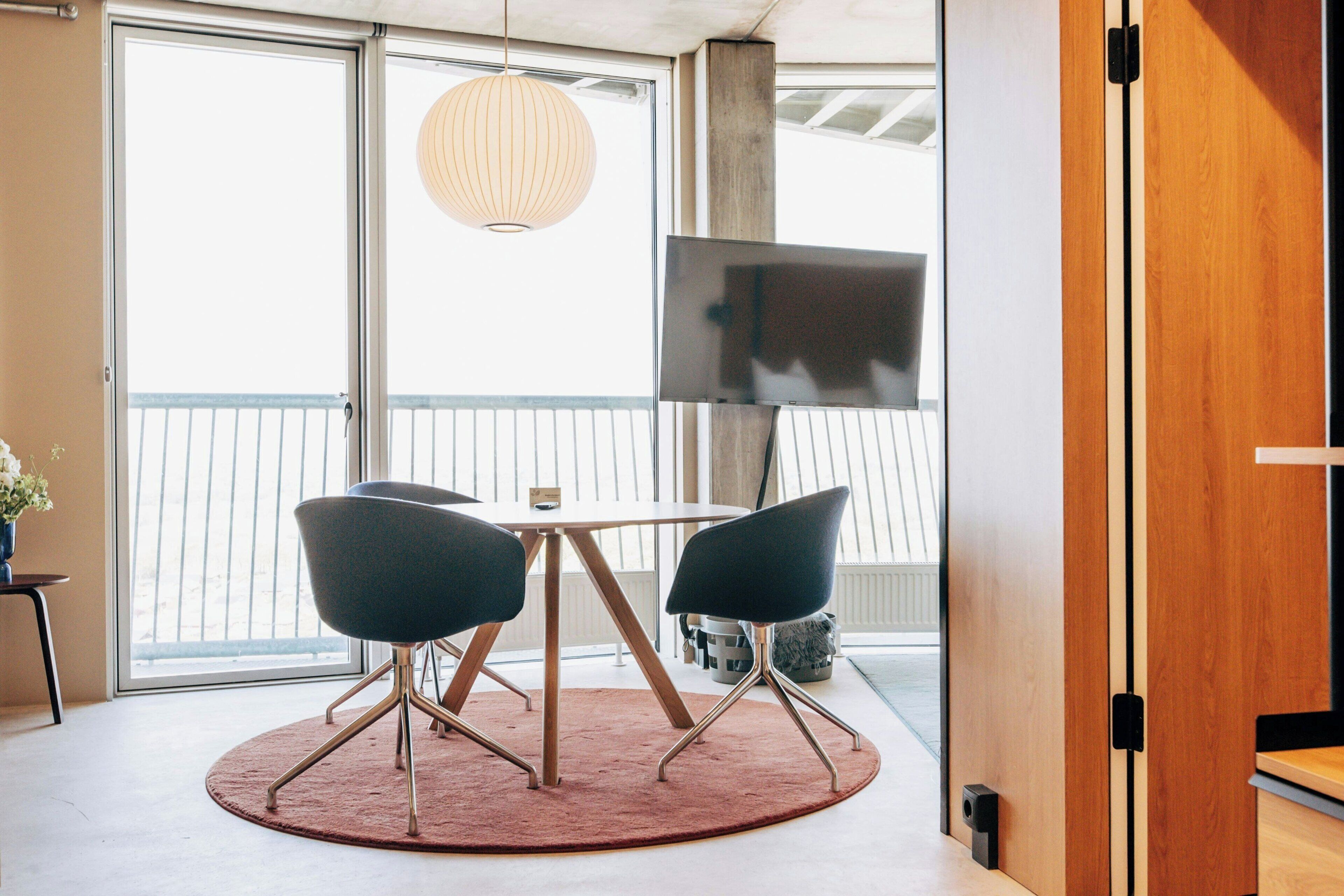 Une chambre moderne avec une table ronde, deux chaises, un téléviseur et une grande fenêtre.