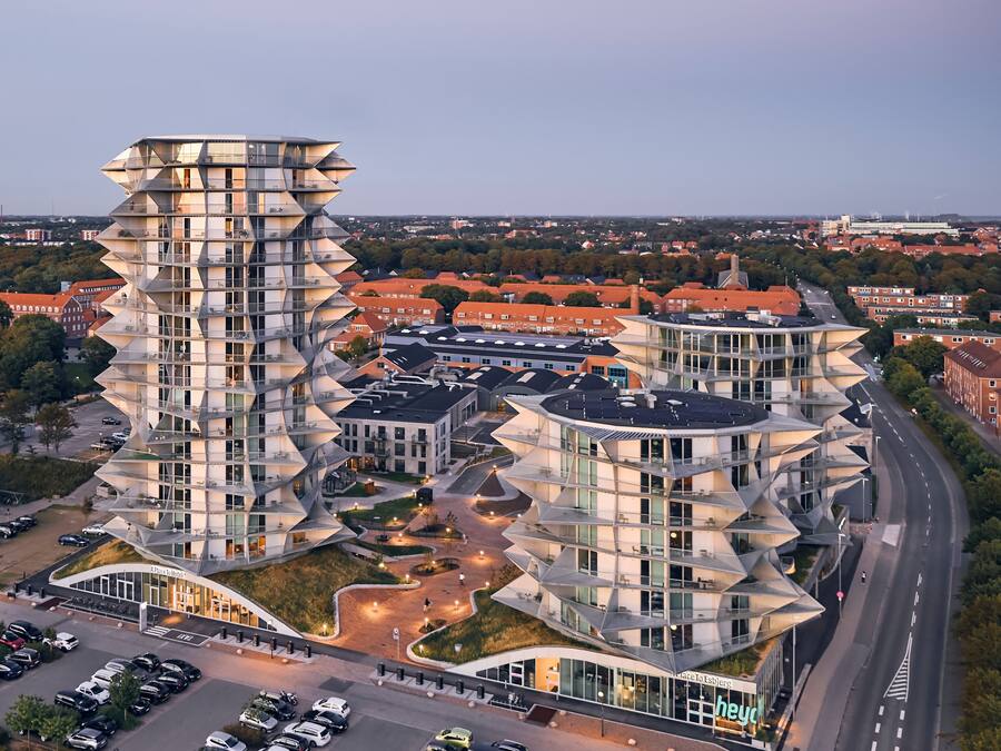A modern hotel with a unique angular design, featuring multiple balconies and a spacious parking area.