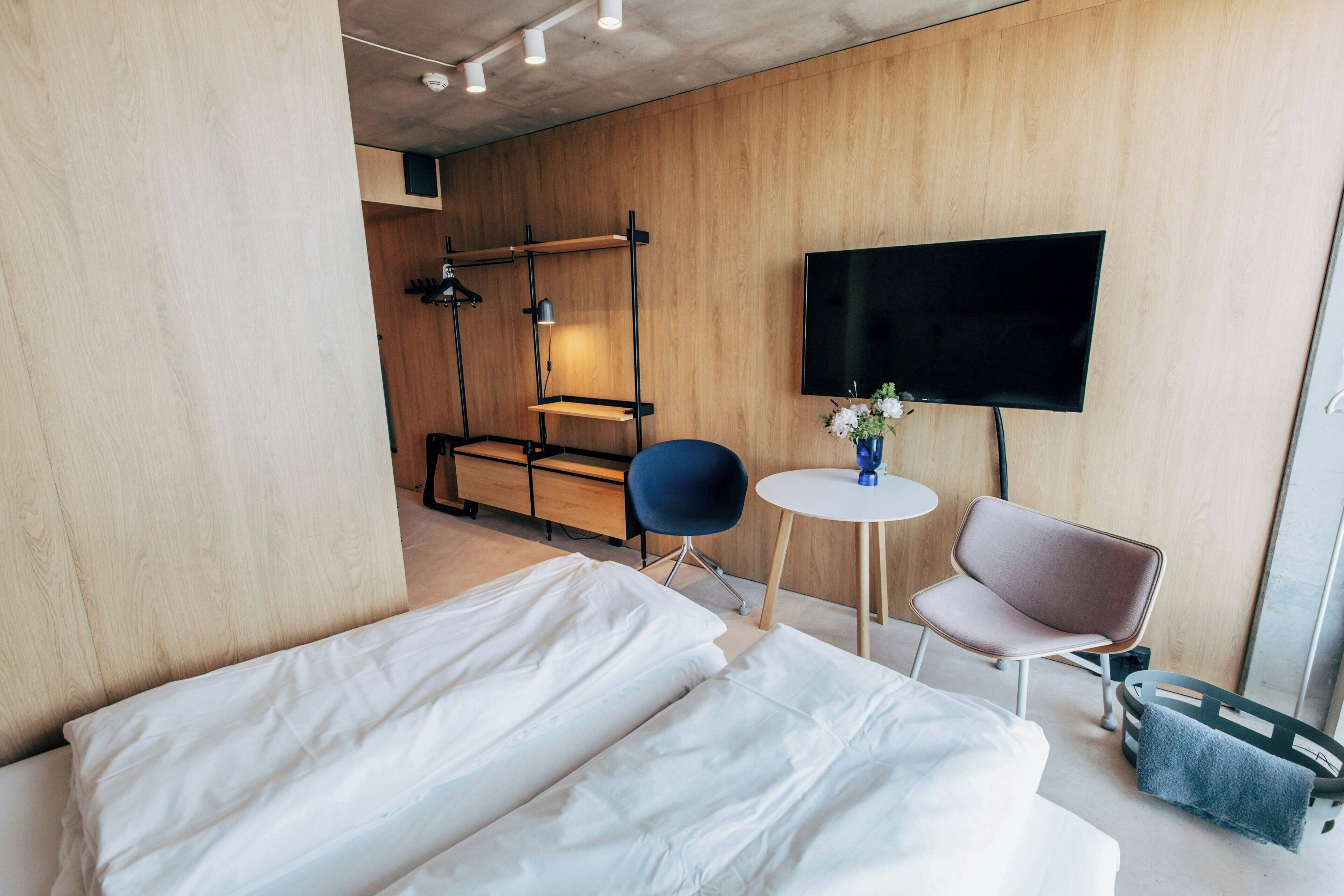 Habitación de hotel con una cama, dos sillas, una mesita, un televisor y una pared de madera.