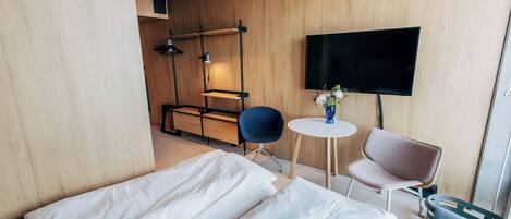 Habitación de hotel con una cama, dos sillas, una mesita, un televisor y una pared de madera.