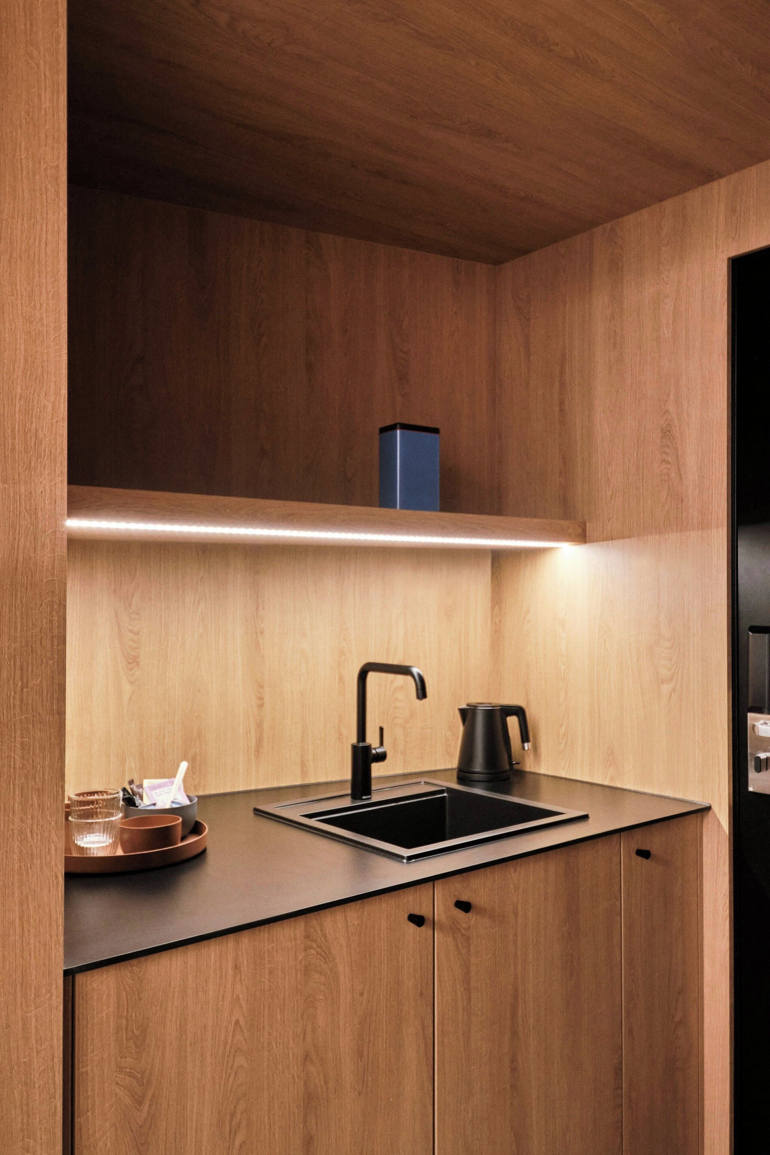 Una cocina moderna con armarios de madera, encimera negra, un lavabo, un hervidor y un pequeño estante sobre el lavabo.