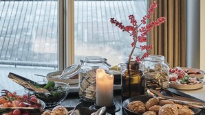 A dining table with various food items and a candle, set against a window with a view of a snowy landscape.