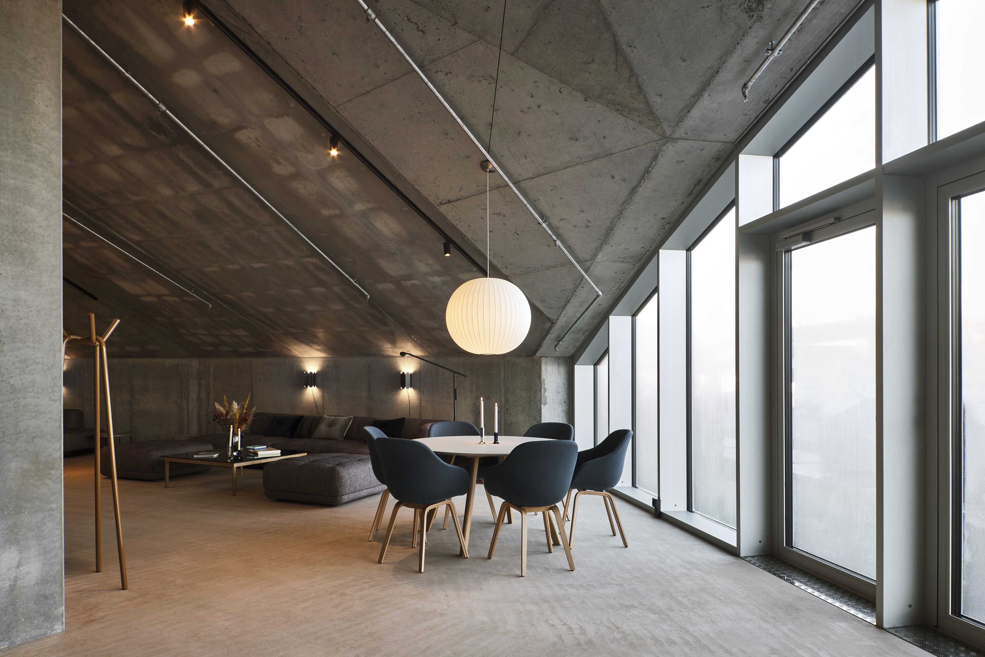 Un interior moderno con zona de comedor que incluye una mesa redonda y sillas, un sofá, y un ventanal que aporta luz natural.