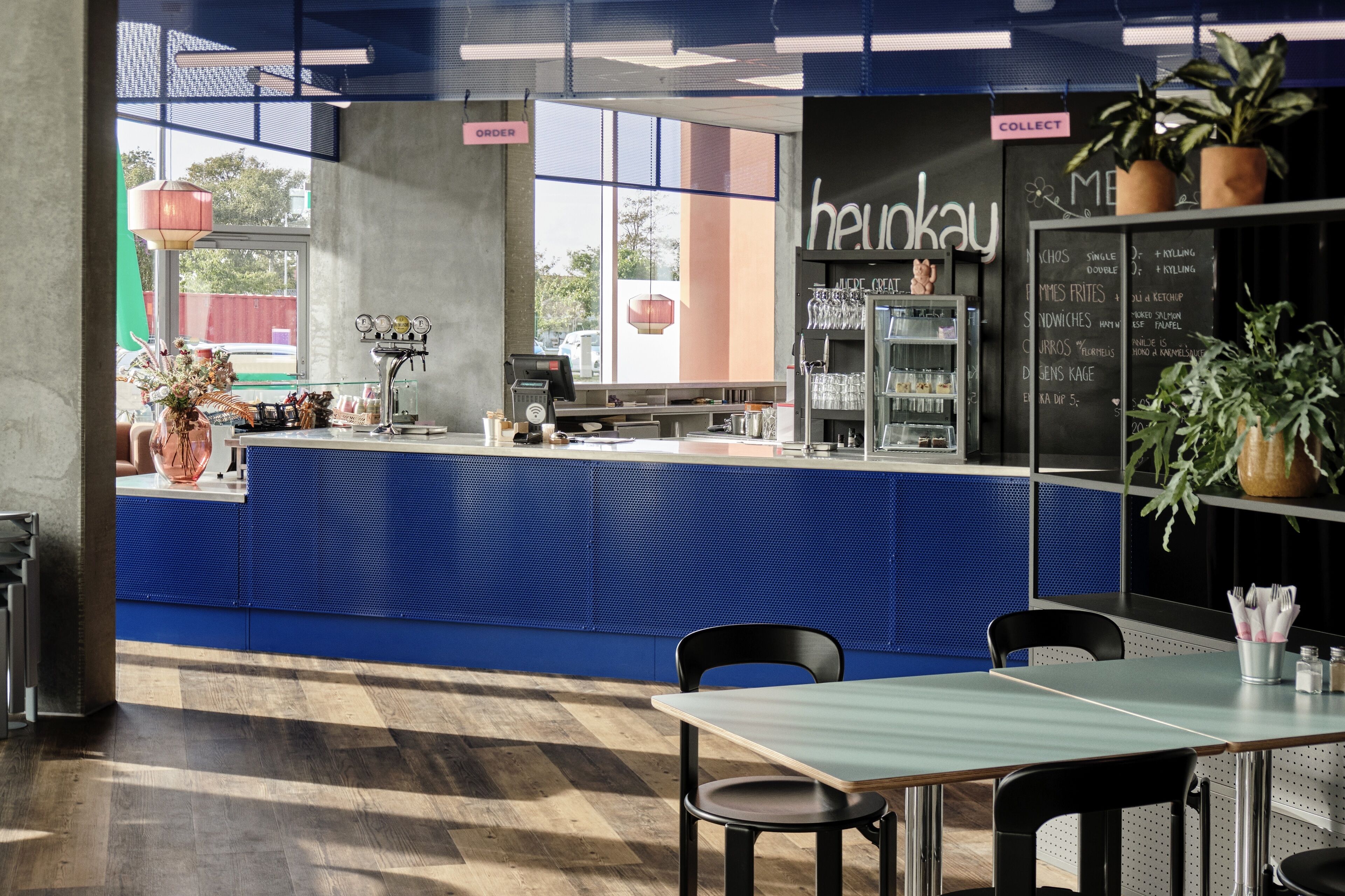 A modern restaurant interior with a blue counter, black chairs, and a menu board.