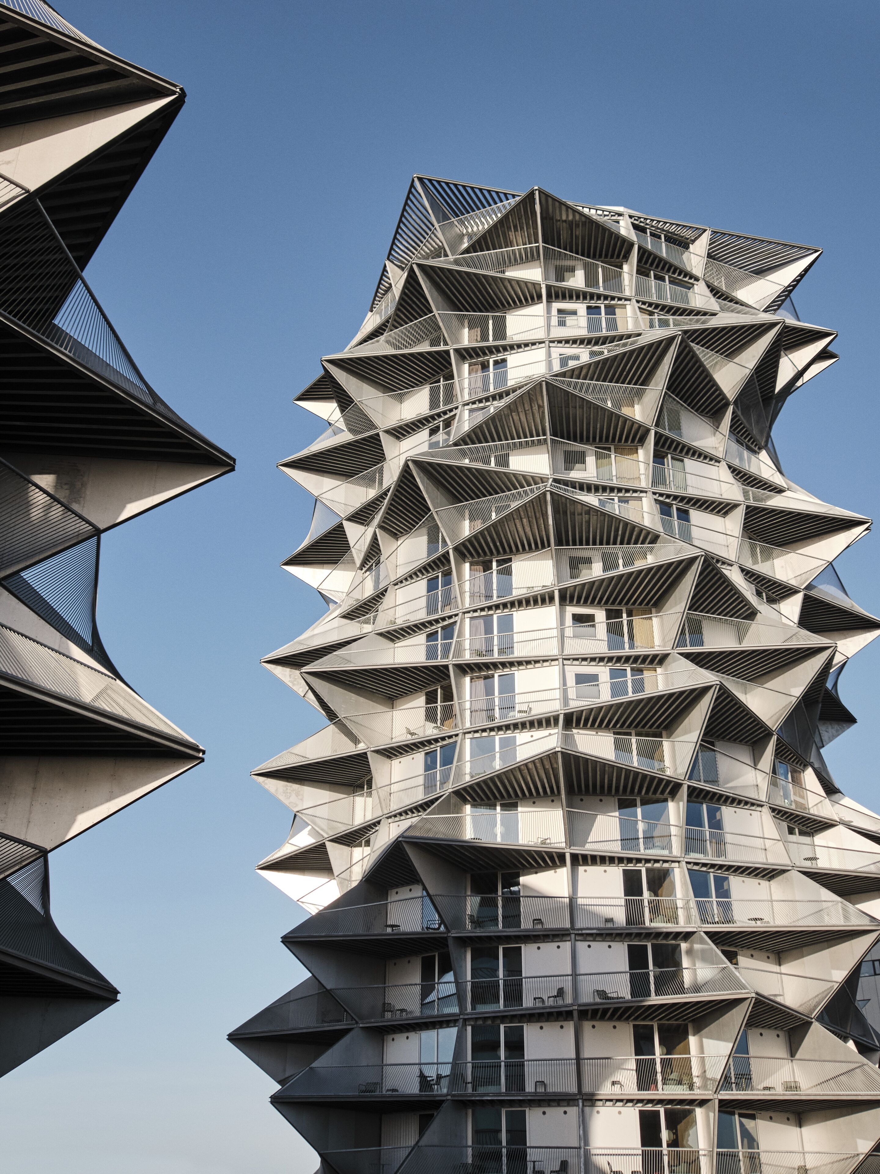 A modern building with a unique angular design, featuring multiple balconies and a clear sky in the background.