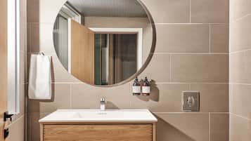 Un baño moderno con un tocador de madera, un espejo redondo, un inodoro y una toalla colgada en la pared.