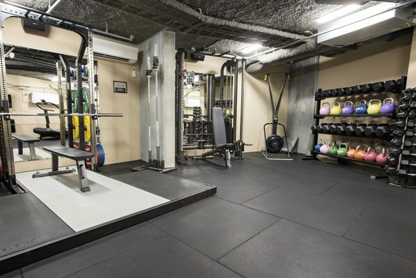 Een sportschool met gewichthefapparatuur, een bank en een rek met kettlebells.