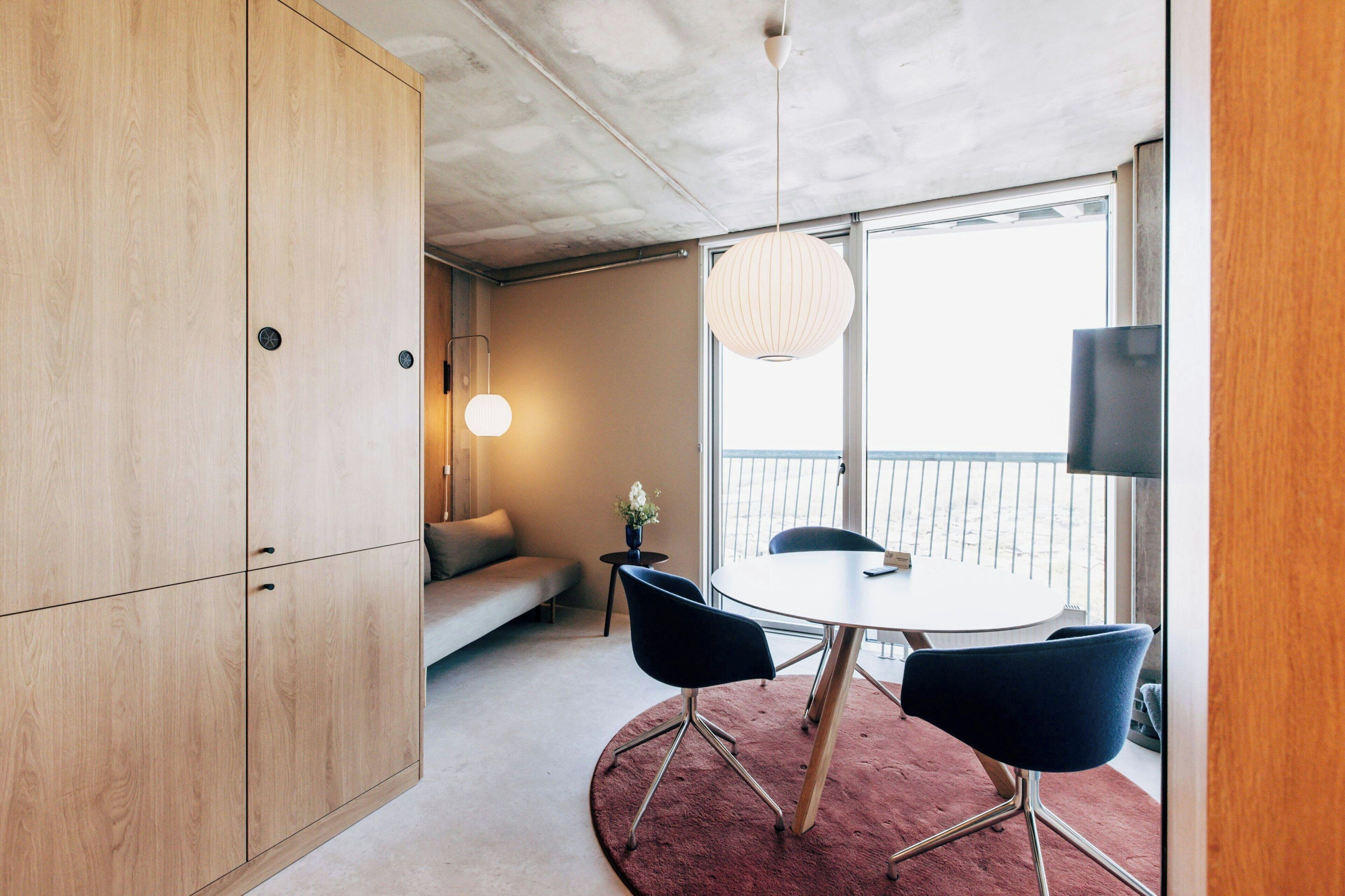 A modern room with a round table, two chairs, a sofa, a small side table, and a hanging light fixture.