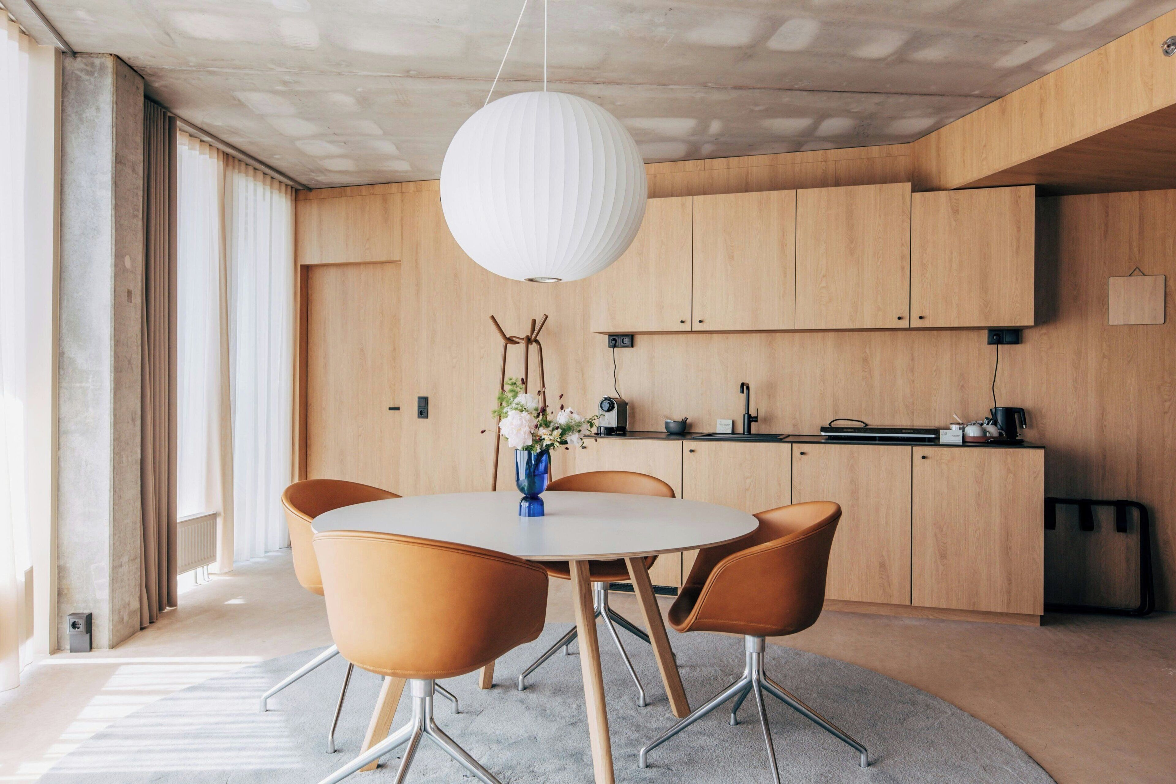 Una cocina moderna con armarios de madera, una mesa redonda con sillas y una lámpara colgante.