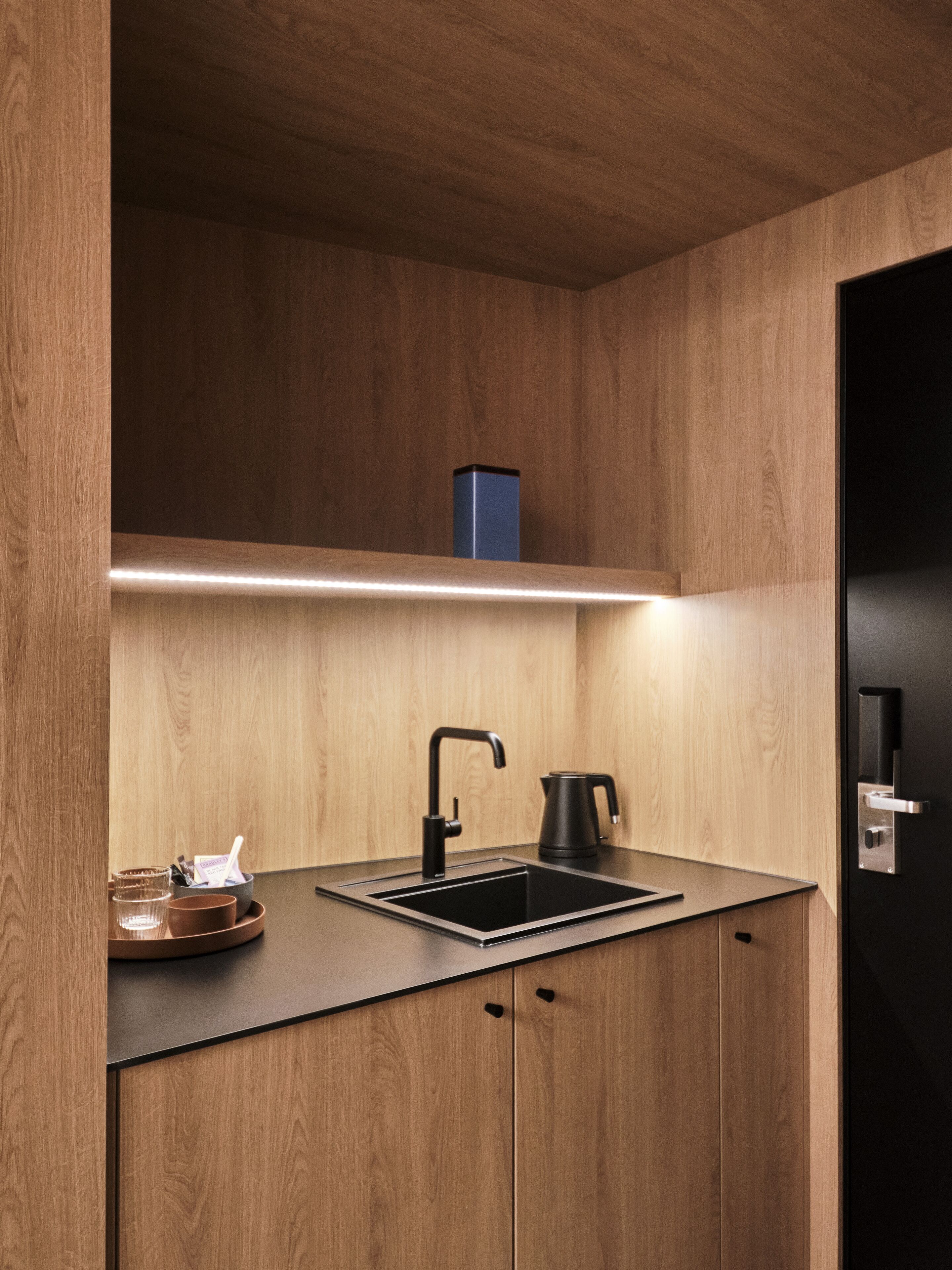 Eine moderne Küche mit Holzschränken, einem schwarzen Spülbecken und einem Wasserkocher.
