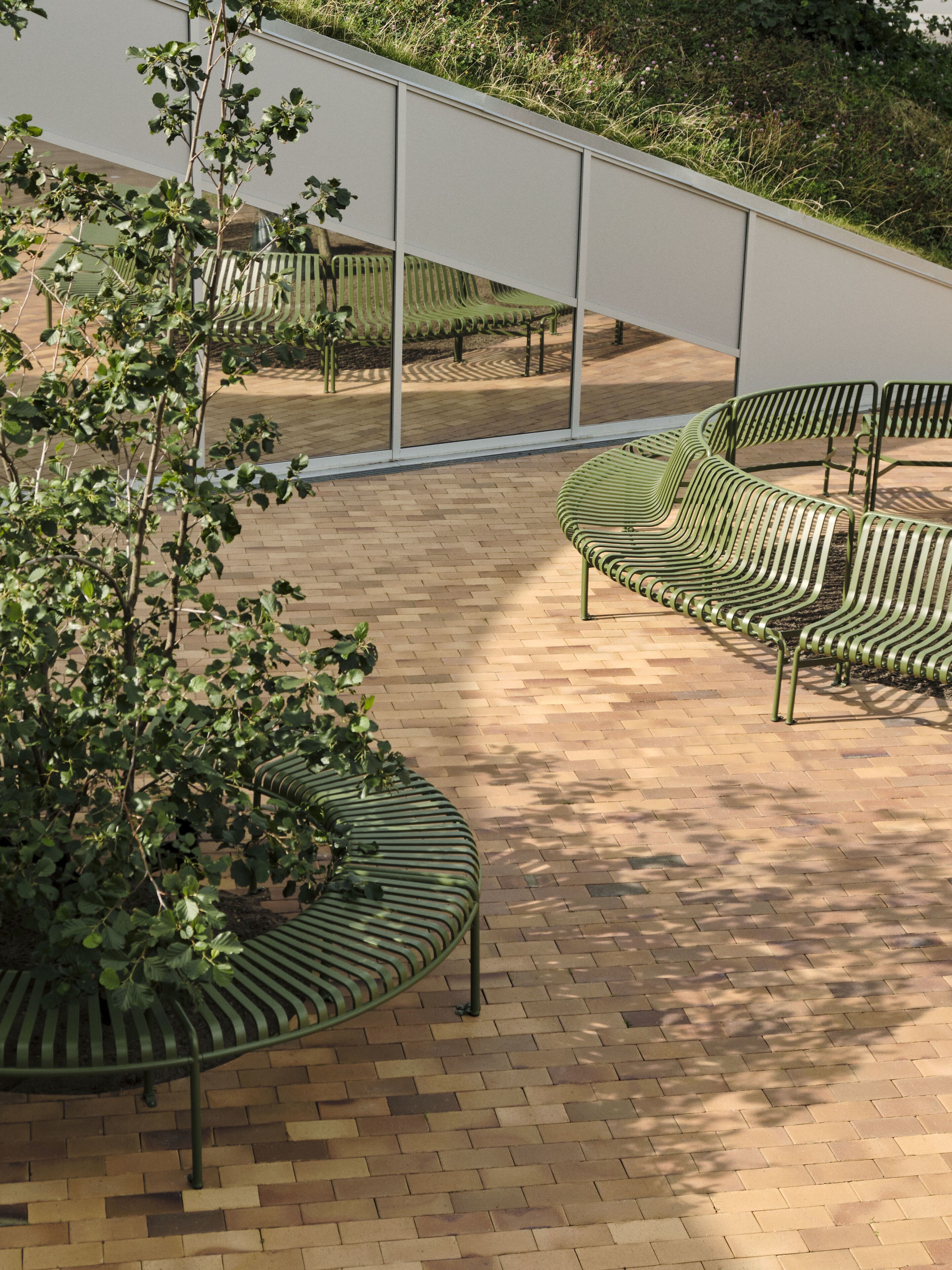 A modern outdoor seating area with green metal benches and a brick floor.