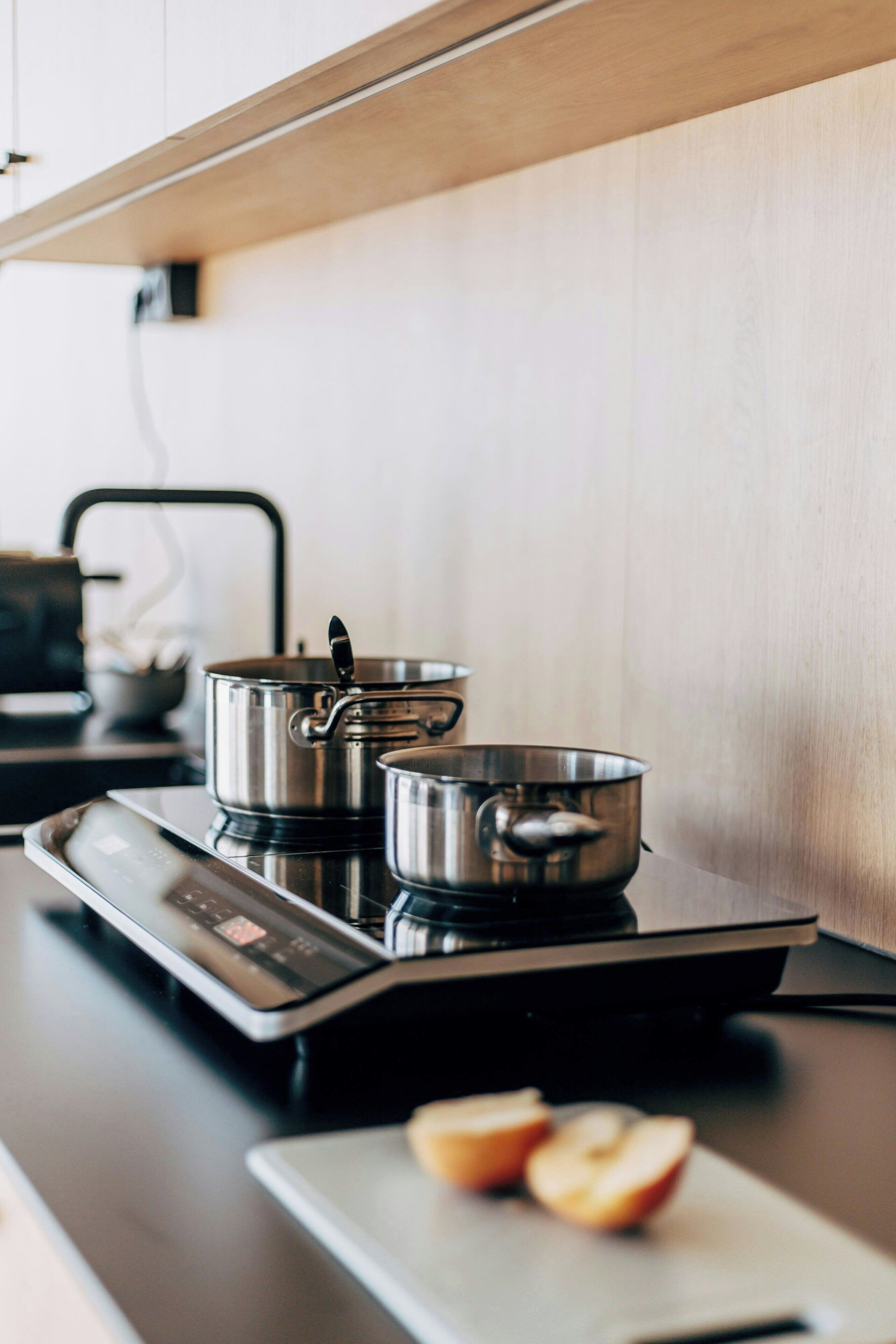 A kitchen with an induction cooktop, two pots, and a cutting board with apple slices.