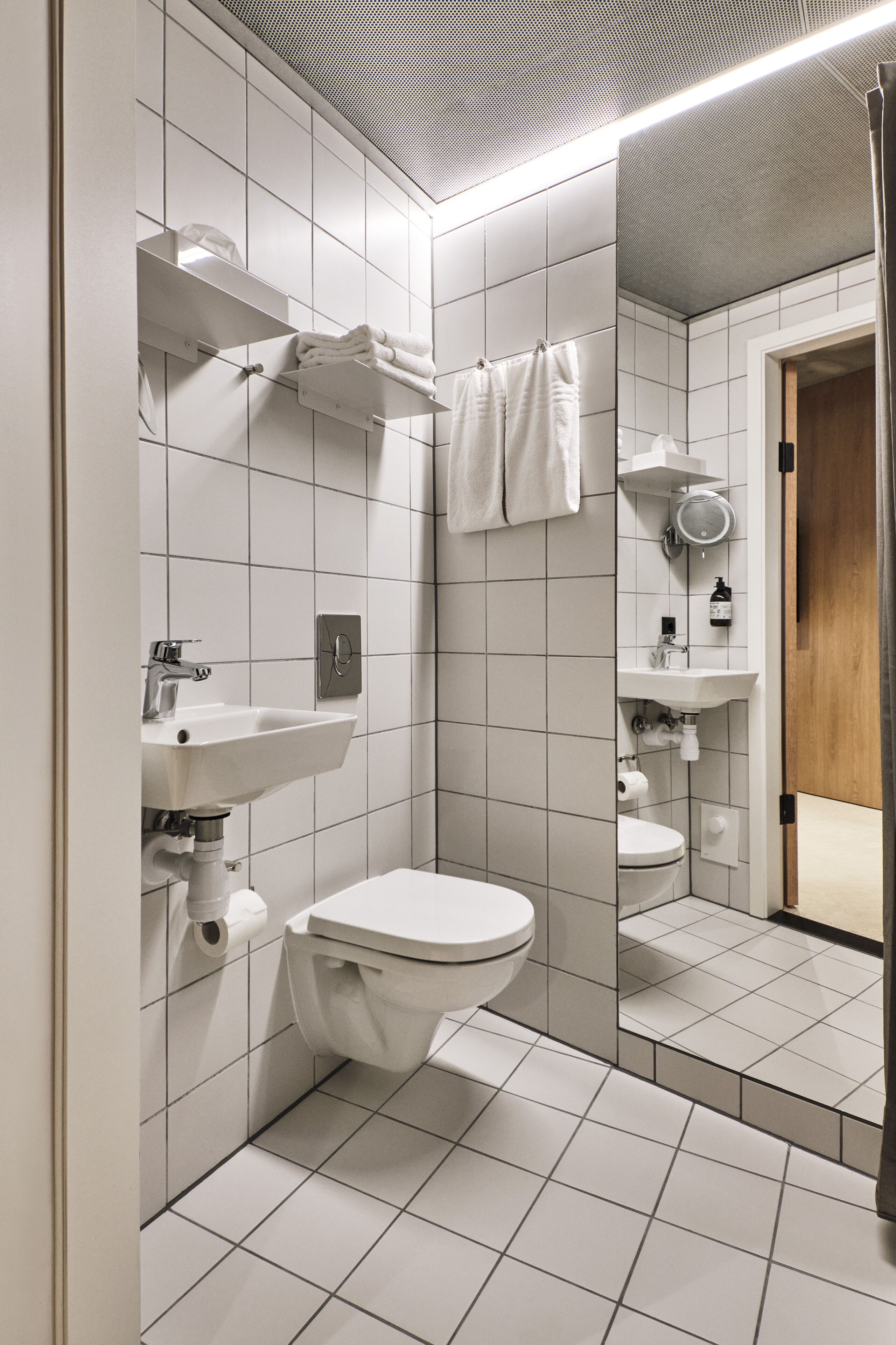 Un bagno moderno rivestito di piastrelle bianche, con lavandino, WC e specchio.
