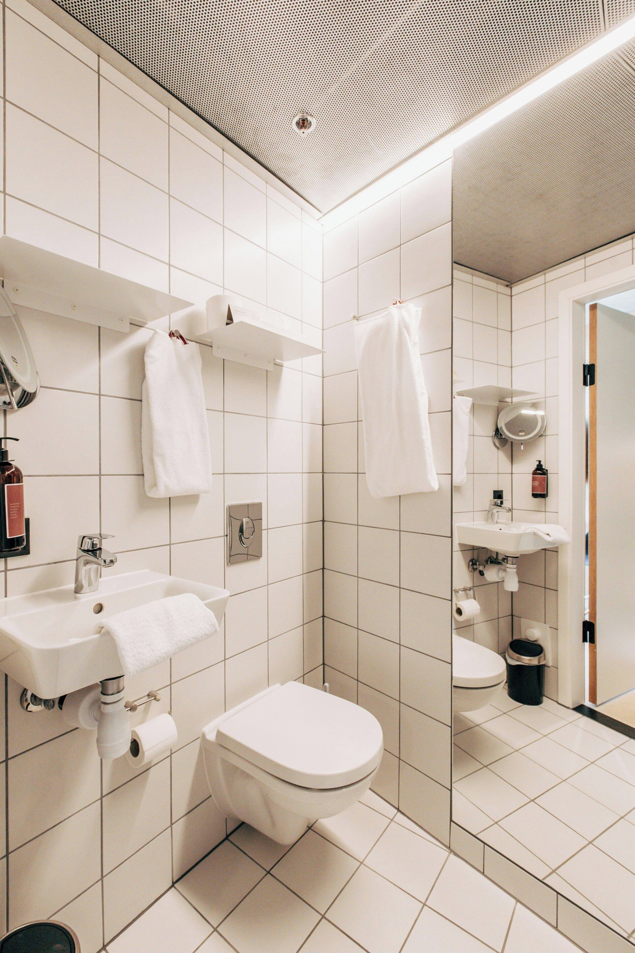 Un baño moderno con azulejos blancos, un lavabo, un inodoro y un espejo.