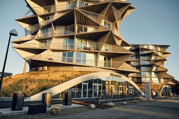 Un edificio moderno con un diseño angular distintivo, que cuenta con varios balcones y una entrada curva.