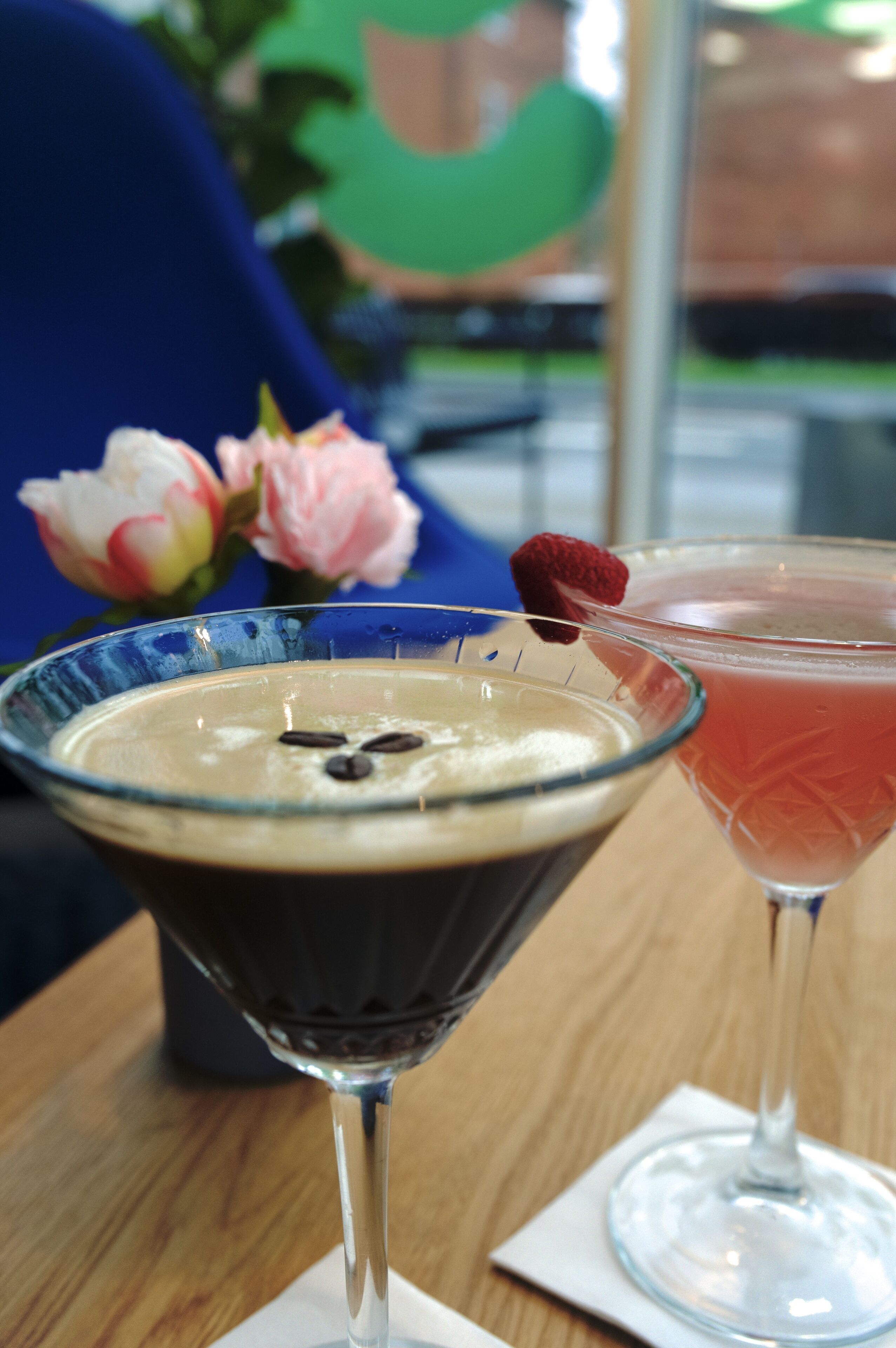 Deux boissons sur une table, avec une chaise bleue et une fleur en arrière-plan.