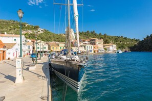 A coastal town with a docked sailboat, buildings along the waterfront, and a hilly backdrop.