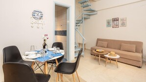 Un coin repas avec une table dressée pour deux personnes, un canapé, une petite table ronde surmontée d’un abat-jour et un escalier en colimaçon bleu.