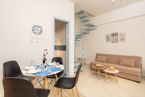 Un comedor con una mesa para dos, un sofá, una pequeña mesa redonda con un sombrero y una escalera en espiral azul.