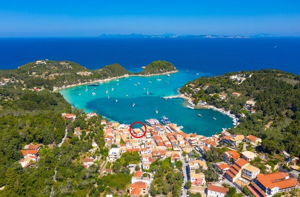 An aerial view of a coastal town with a marina, surrounded by hills and clear blue waters.