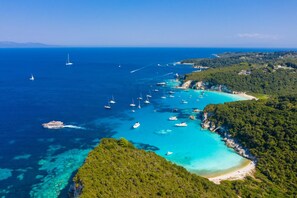 An aerial view of a coastal area with clear turquoise waters, numerous boats, and lush green hills.