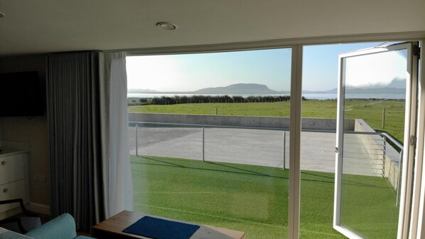 A hotel room with a large sliding glass door leading to a balcony with a view of a grassy field and a distant mountain.