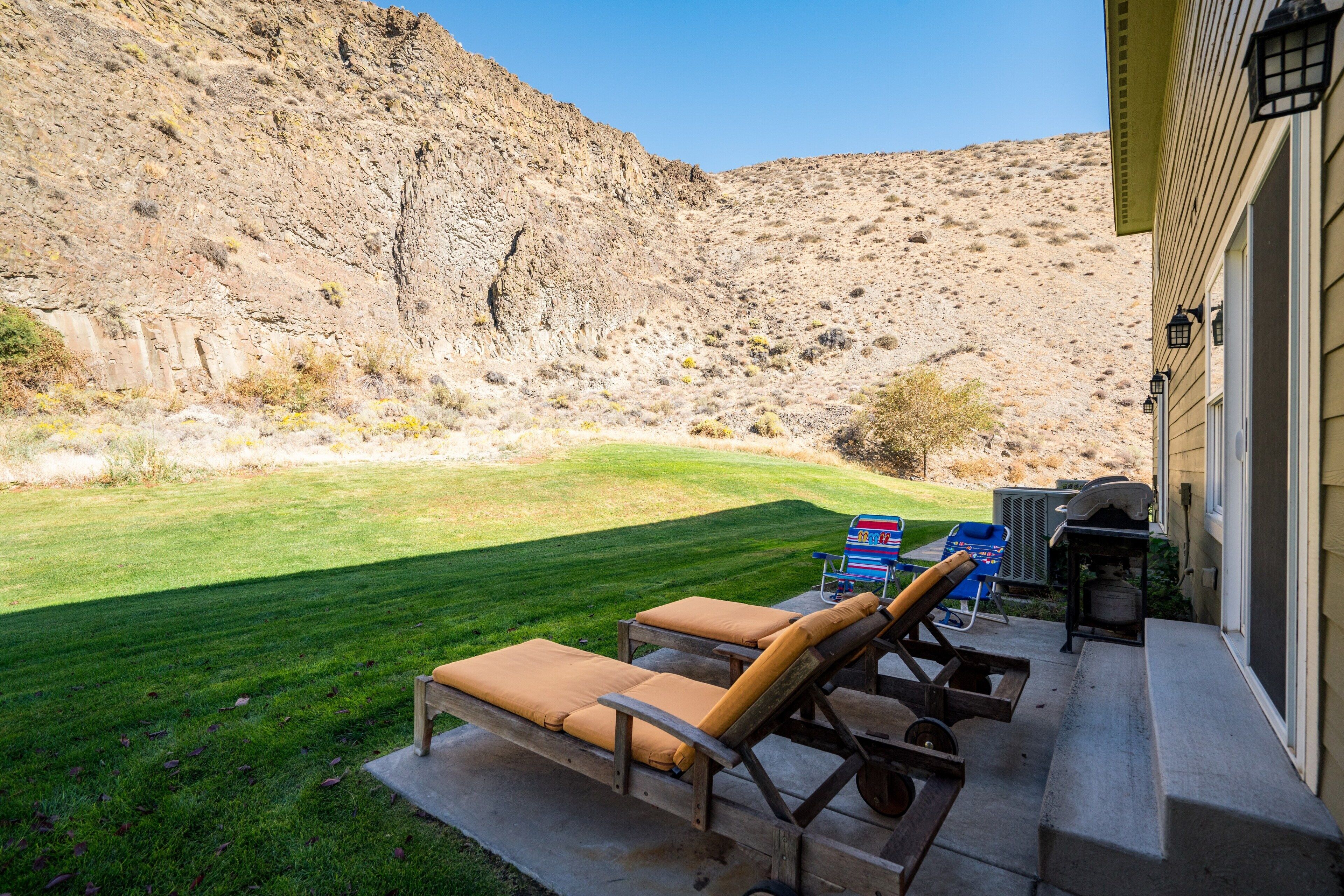 A patio with two lounge chairs, a grill, and a small table.