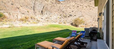 A patio with two lounge chairs, a grill, and a small table.