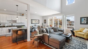 A spacious living area with a grey sectional sofa, a yellow armchair, and a kitchen with white cabinets and a bar area. - Luxury @ Crescent Bar! Pool & Free Golf! (Quincy)