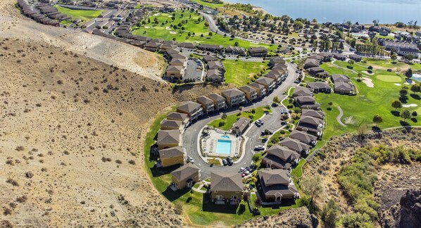 An aerial view of a residential area with houses arranged in a semi-circular pattern around a central swimming pool, with the Columbia River visible in the background.