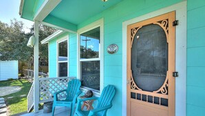 A turquoise house with a porch, two Adirondack chairs, and a wooden door with a screen.