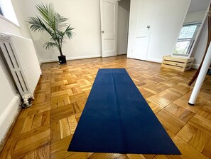 Quarto com piso de parquet de madeira, um tapete de exercícios azul, uma planta em vaso e um radiador.