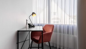 Une chambre d’hôtel équipée d’un bureau, d’une chaise, d’une lampe et d’une fenêtre avec des rideaux légers.