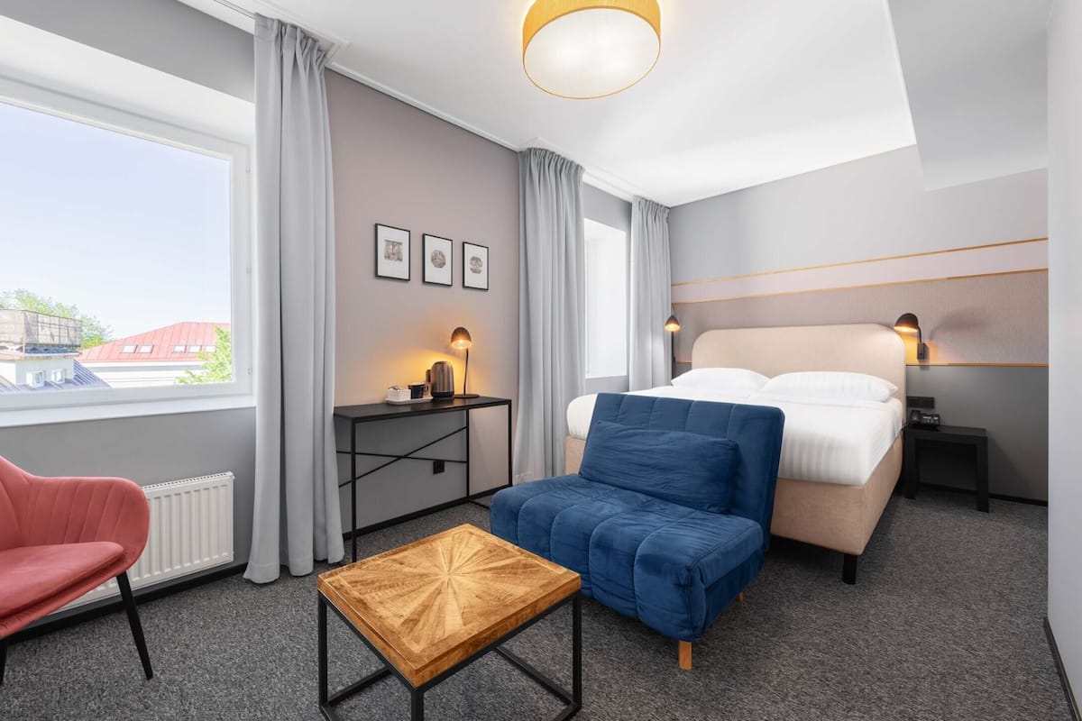 A modern hotel room with a bed, a desk, a chair, and a small table.