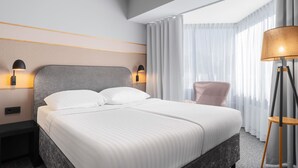 Une chambre d’hôtel moderne avec un grand lit, deux lampes de chevet, une chaise et une lampe sur pied.
