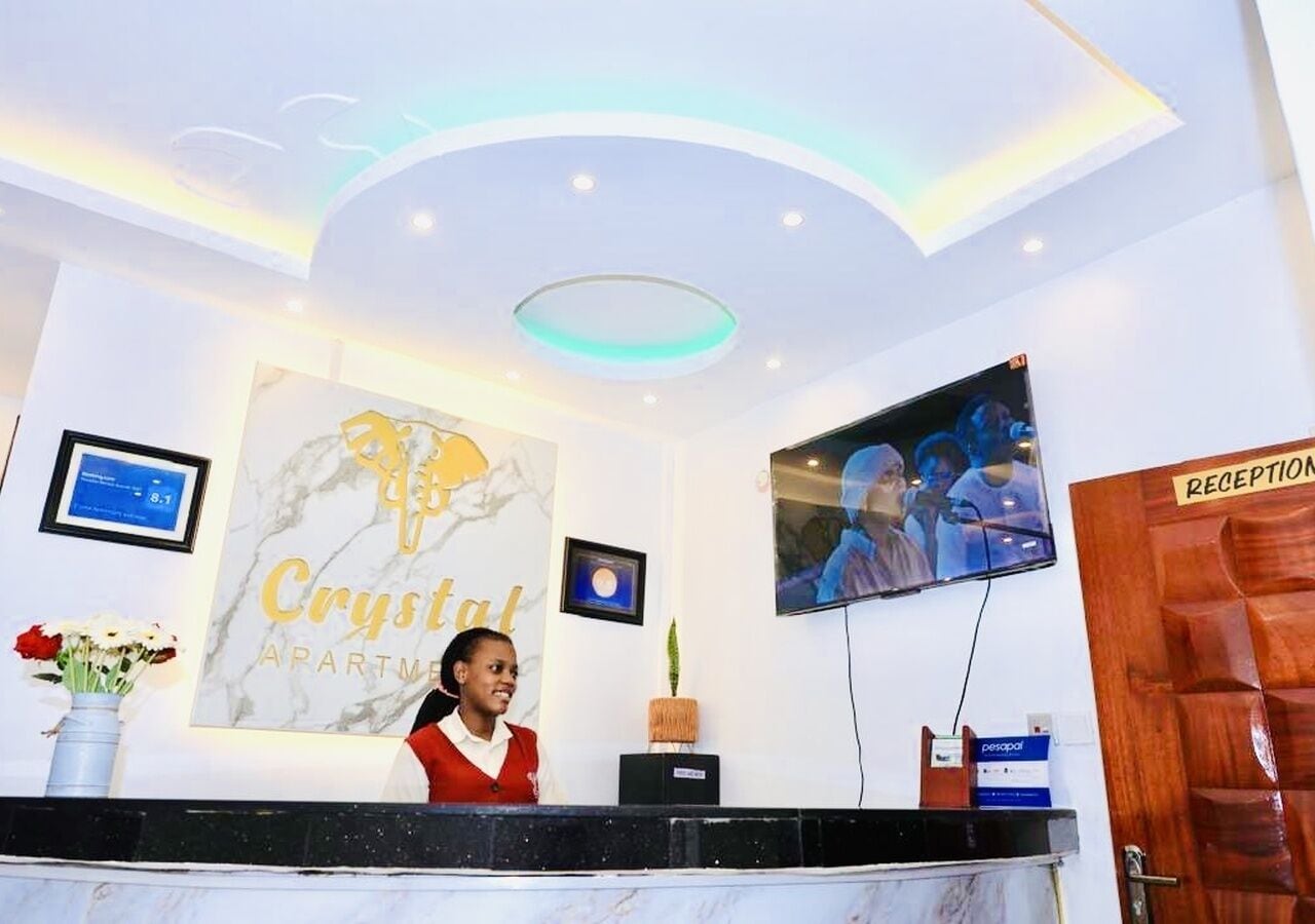 Un comptoir d’accueil avec une enseigne indiquant « Crystal Apartments », un téléviseur et un espace d’attente.