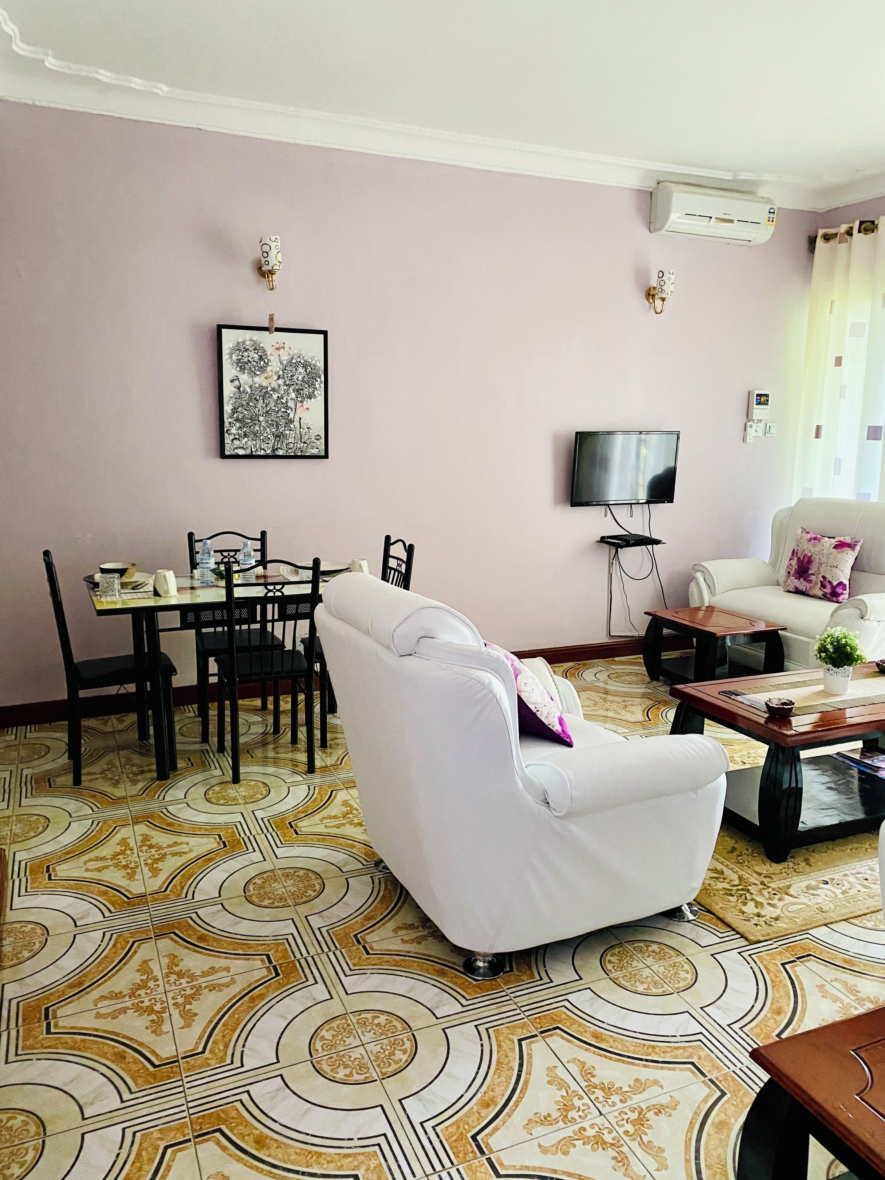 Una sala de estar con un sofá blanco, una mesa de comedor con sillas, un televisor y un piso con diseño.